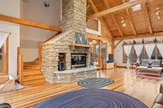 Spacious living room with high ceilings, wooden beams, large stone fireplace, and elegant wood flooring.