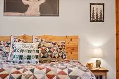 Cozy bedroom with quilted bedding, decorative pillows, wooden headboard, wall art, and a bedside table with a lamp.