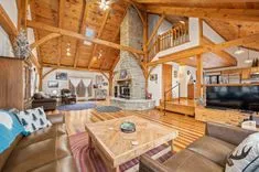 Spacious living room in a cabin-style home with a high wooden ceiling, stone fireplace, and hardwood floors.