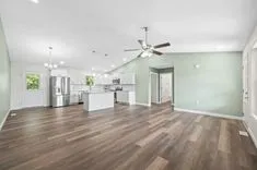 Spacious and modern kitchen interior with stainless steel appliances, white cabinetry, and hardwood floors, accented with light green walls and ample natural light.