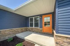 Modern house exterior with navy blue siding, stone veneer, and a bright orange front door with a large window.