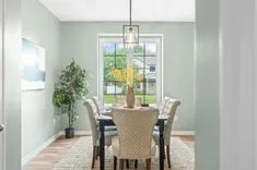 Elegant dining room interior with a table set for four, pendant light, and a view of the backyard through large windows.