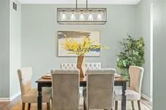 Elegant dining room with a modern chandelier, a wooden table with mixed chair styles, and a painting of a tree above a console table.