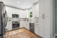 Modern kitchen interior with white cabinetry, stainless steel appliances, and hardwood floors.