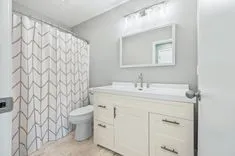 Modern bathroom interior with geometric patterned shower curtain, white vanity cabinet, and mirror.