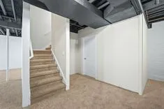 Interior of an empty room with white walls, a staircase, and exposed ductwork on the ceiling.