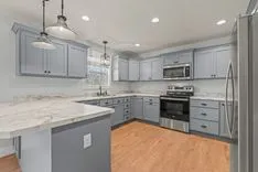 Modern kitchen interior with light gray cabinetry, stainless steel appliances, marble countertops, and hardwood flooring.