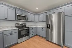 Modern kitchen interior with gray cabinets, stainless steel appliances, and hardwood floor.