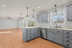 Modern kitchen with gray cabinets, stainless steel appliances, white countertops, and pendant lights over an island.