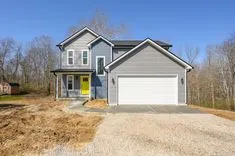 New two-story house with blue siding, white garage door, and bright yellow front door, on a clear day with surrounding bare trees and unfinished landscaping.