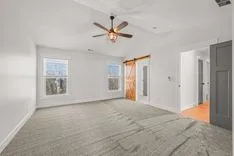 Empty modern room with carpeted floor, white walls, ceiling fan, and a barn-style sliding door.