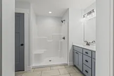 Modern bathroom interior with white shower stall, blue vanity cabinet with sink, and wall-mounted lights.
