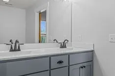Modern bathroom interior with a double sink, gray vanity cabinet, and a mirror reflecting a window.