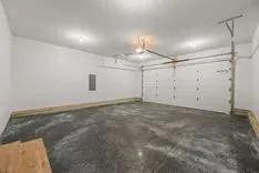 Empty two-car garage interior with white walls, closed garage door, and stained concrete floor.