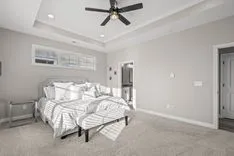 Bright and airy bedroom with a large bed, white and gray bedding, ceiling fan, and a glimpse into the en-suite bathroom.