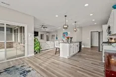 Modern open concept living space with kitchen island, dining and living areas, and sliding glass door to outdoor patio.