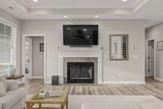 Modern living room interior with a plush sofa, wooden coffee table, a fireplace with a mounted television above it, and decorative accents, in a neutral color palette.
