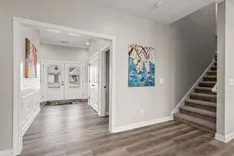 Interior of a modern home entryway with a staircase, wood flooring, artwork on the walls, and a front door with sidelights.