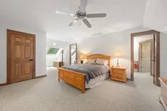 Spacious bedroom with large bed, wooden furniture, carpeted flooring, and a ceiling fan.