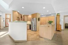 Bright modern kitchen interior with light wood cabinetry, stainless steel appliances, and a central island.