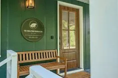 Entrance of 'The Bullfrog Bungalow' with a dark green exterior wall, wooden door, bench, and a circular sign depicting a frog.