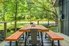 Wooden picnic table and benches on an outdoor deck with green trees in the background.
