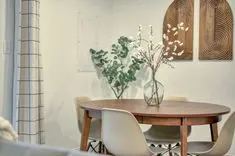 Modern dining room with a wooden table, white chairs, decorative vase with white flowers, and abstract wall art.