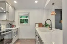 Modern kitchen interior with white cabinets, stainless steel appliances, a marble countertop, and a copper pendant light.