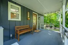 Cozy covered house porch with wooden bench, welcome mat, and a view of green trees in the yard.