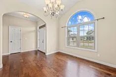 Empty room with polished hardwood floors, large arched window, chandelier, and open doors.