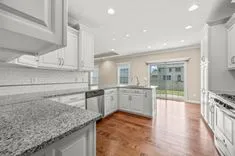Bright contemporary kitchen with white cabinetry, stainless steel appliances, granite countertops, and hardwood floors.