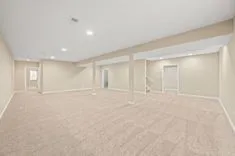 Spacious empty basement room with carpeted floors and recessed lighting.