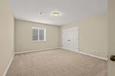 Empty room with beige carpet, white walls, one window, and a closed white door.