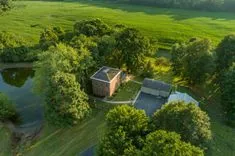 Aerial view of a brick house next to a pond surrounded by trees with adjacent farmland during the golden hour.