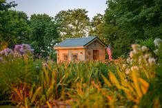 A quaint garden shed with an American flag surrounded by lush, colorful flowers at dusk.