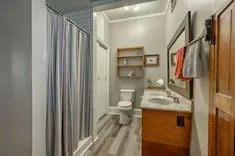 Modern bathroom interior with striped shower curtain, wooden cabinet-sink combo, mirror, toilet, and shelving with towels and decor.
