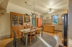 Cozy vintage kitchen and dining area with wooden furniture, a china cabinet, and round chandelier, with sunlight shining through windows.