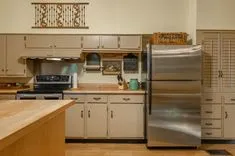 A well-lit traditional kitchen featuring beige cabinets, stainless steel refrigerator, stove, wooden countertop island, and decorative elements.