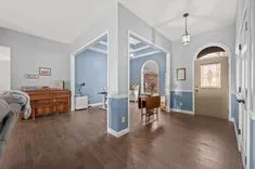 Elegantly designed interior of a home with hardwood floors, pale blue walls, white trim, a wooden desk with a chair and a piano in the living area, and a lit pendant lamp over the entrance with a glass panel door.
