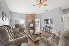 Spacious living room with a brick fireplace, plush sofas, hardwood floors, and sliding doors leading to an outdoor area.