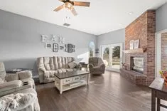 Bright living room with plush sofas, hardwood floors, a brick fireplace, and decorative 'FAM' letters on the wall.