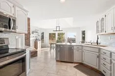 Bright and spacious kitchen with white cabinetry, stainless steel appliances, a brick accent wall, and a dining nook overlooking the backyard.