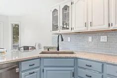 Modern kitchen interior with white upper cabinets and blue lower cabinets, granite countertops, and a subway tile backsplash.