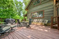 Spacious wooden deck with outdoor furniture, barbecue grill, and lush green trees in the background.