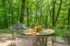 Outdoor picnic table set with plates and food in a wooded campsite with a tent in the background.