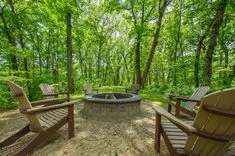 Outdoor fire pit area with Adirondack chairs surrounded by green forest.