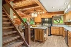 Rustic wooden kitchen interior with granite countertops, wooden cabinets, and wooden stairs leading to the next floor.