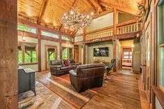Spacious rustic living room with high ceilings, leather furniture, and antler chandelier, with a loft area above.