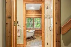 Rustic bathroom interior with clawfoot tub and walk-in shower, viewed through an open wooden door.