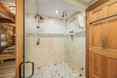 Spacious bathroom with a walk-in tiled shower, glass door, and wooden accents.